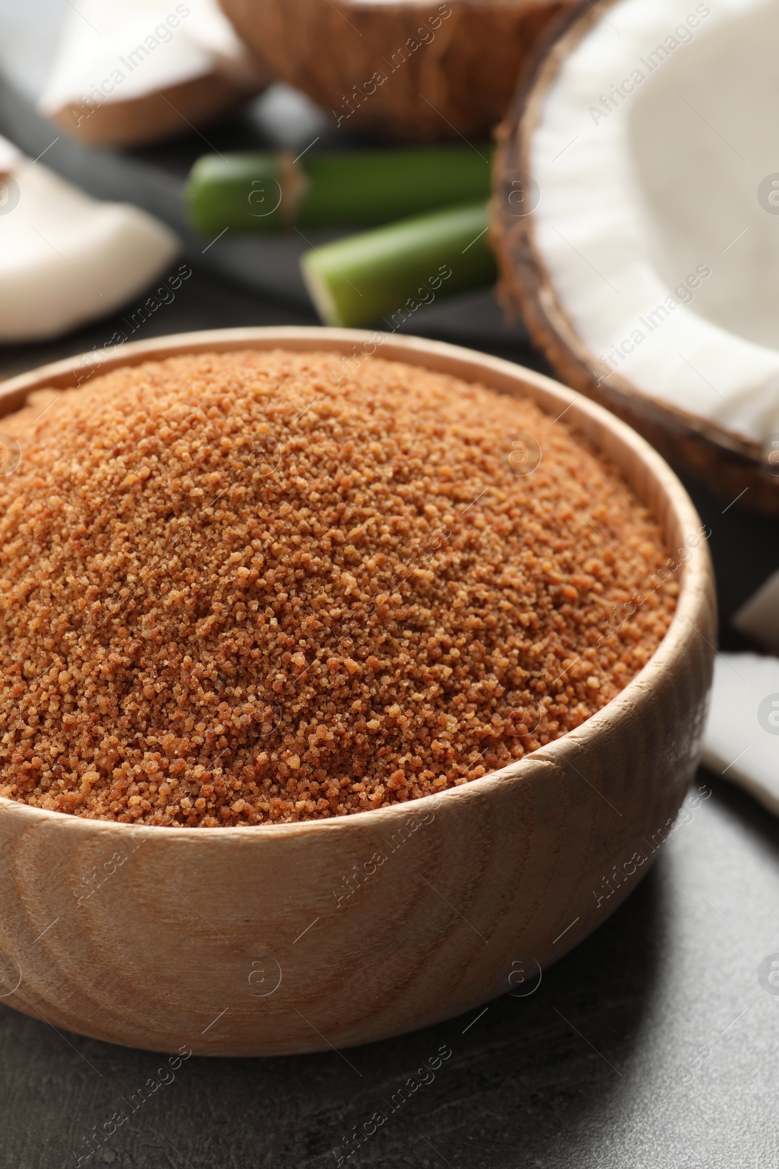 Photo of Natural coconut sugar in wooden bowl on grey table, closeup
