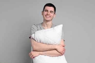 Happy man in pyjama holding pillow on grey background