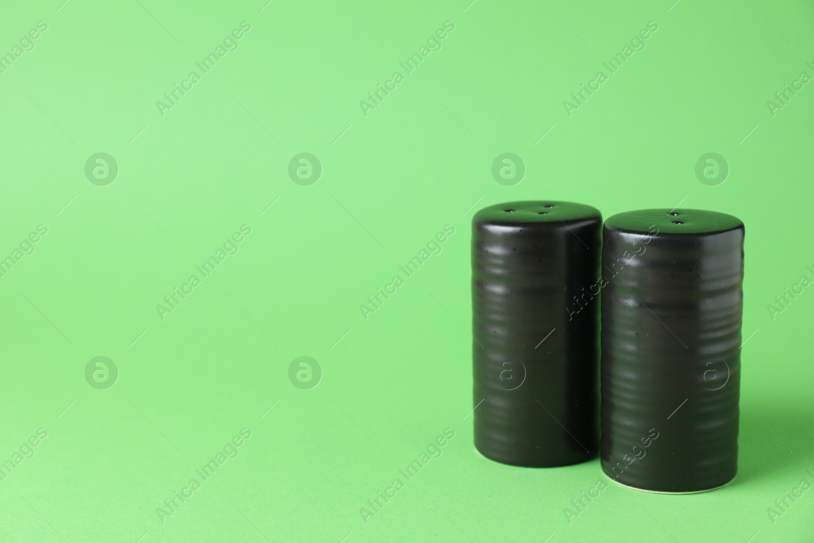 Photo of Black salt and pepper shakers on green background. Space for text