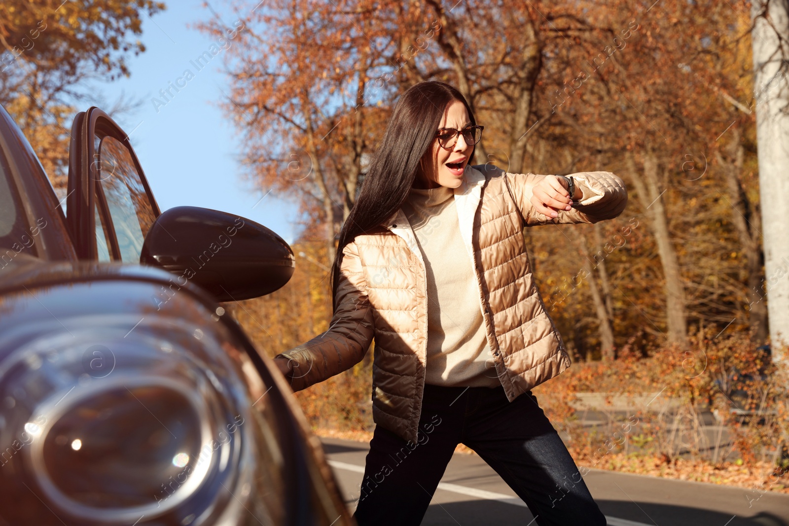 Photo of Emotional woman checking time on watch near car. Being late concept