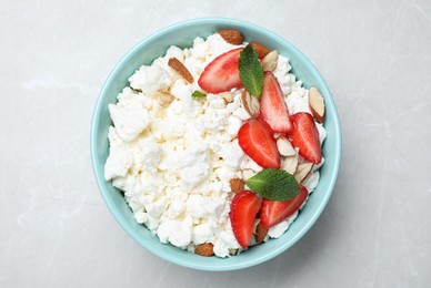 Photo of Fresh cottage cheese with strawberry and almond in bowl on light marble table, top view