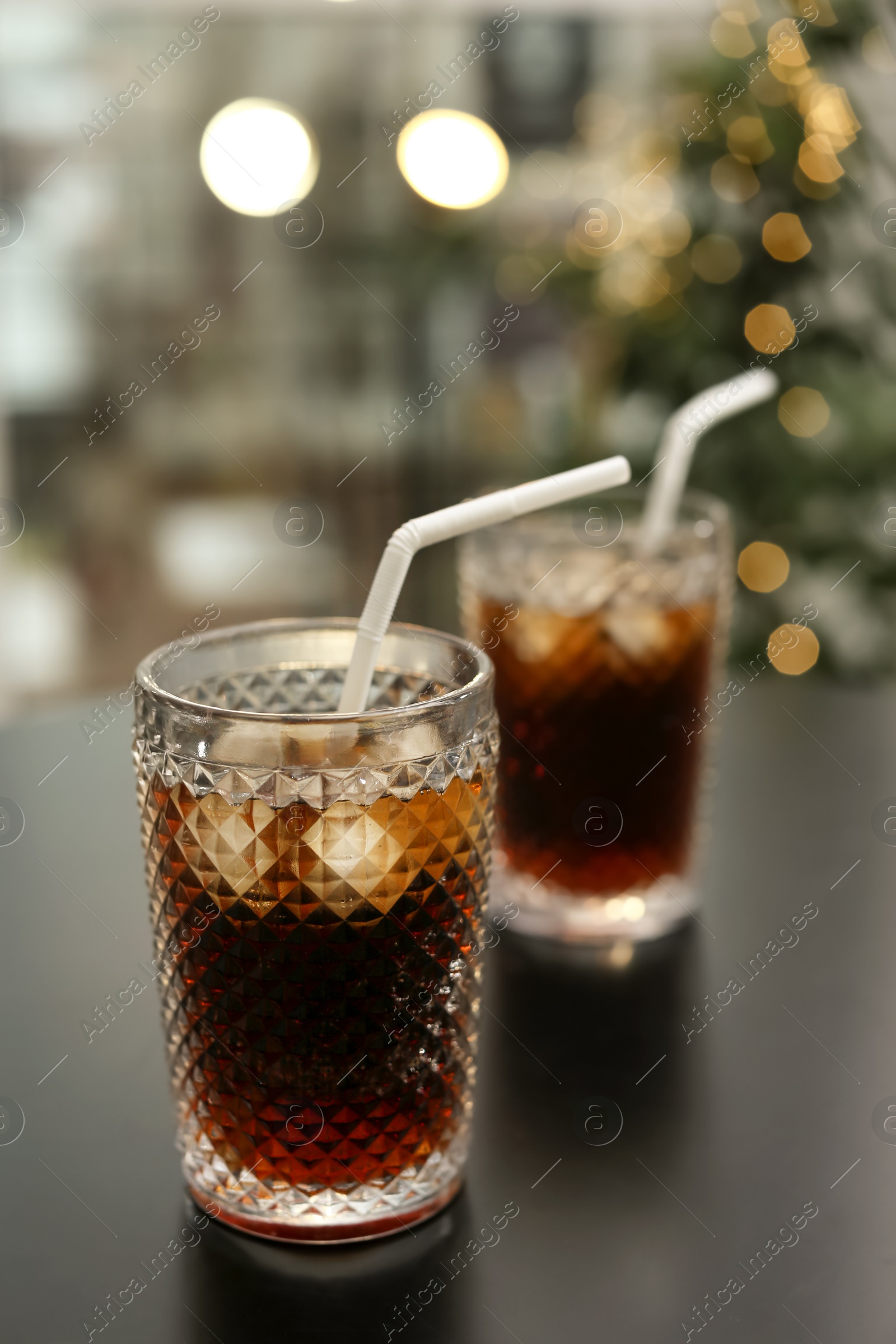 Photo of Glasses of cold cola on table against blurred background