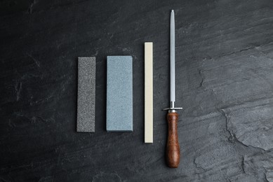 Photo of Sharpening stones and honing steel on black table, flat lay