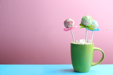 Photo of Tasty cake pops in cup with marshmallow on light blue table against lilac background. Space for text