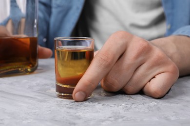 Photo of Alcohol addiction. Man with whiskey at grey textured table, closeup