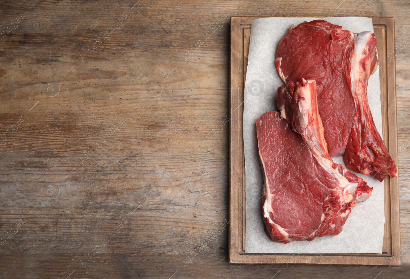 Photo of Fresh raw beef cut on wooden table, top view. Space for text