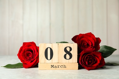 Photo of Wooden block calendar with date 8th of March and roses on table against light background, space for text. International Women's Day
