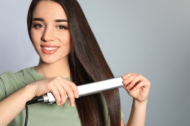 Photo of Happy woman using hair iron on grey background. Space for text