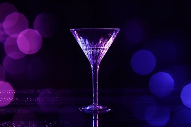 Photo of Martini glass and splashes in neon lights on dark background, bokeh effect