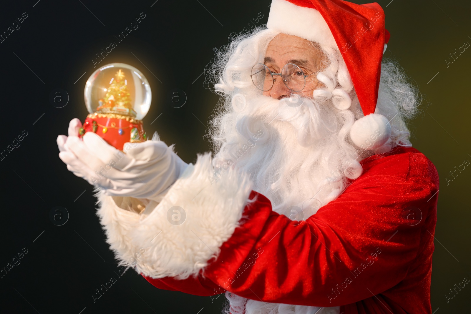 Photo of Merry Christmas. Santa Claus with snow globe on dark background