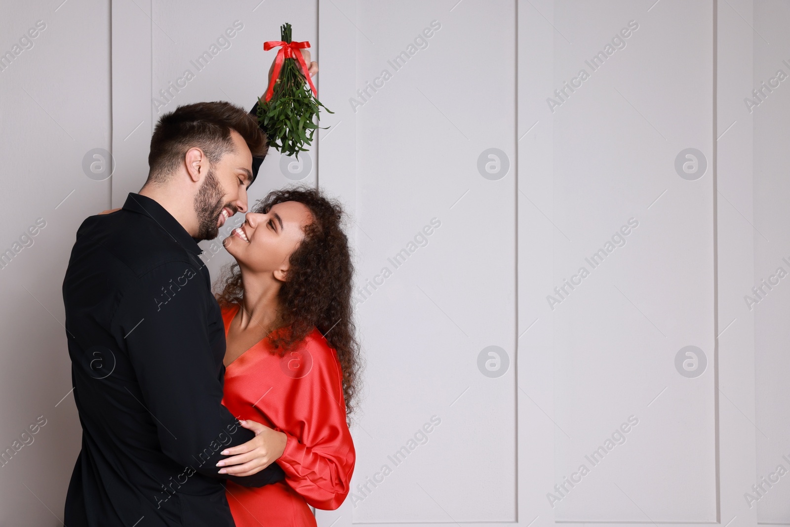 Photo of Lovely couple under mistletoe bunch near light grey wall. Space for text