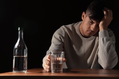 Photo of Addicted man with alcoholic drink at wooden table against black background