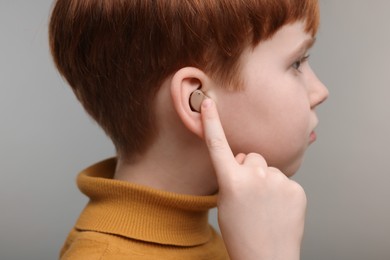 Photo of Little boy with hearing aid on grey background, closeup