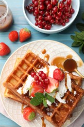 Photo of Delicious Belgian waffles with berries and caramel sauce served on turquoise wooden table, flat lay