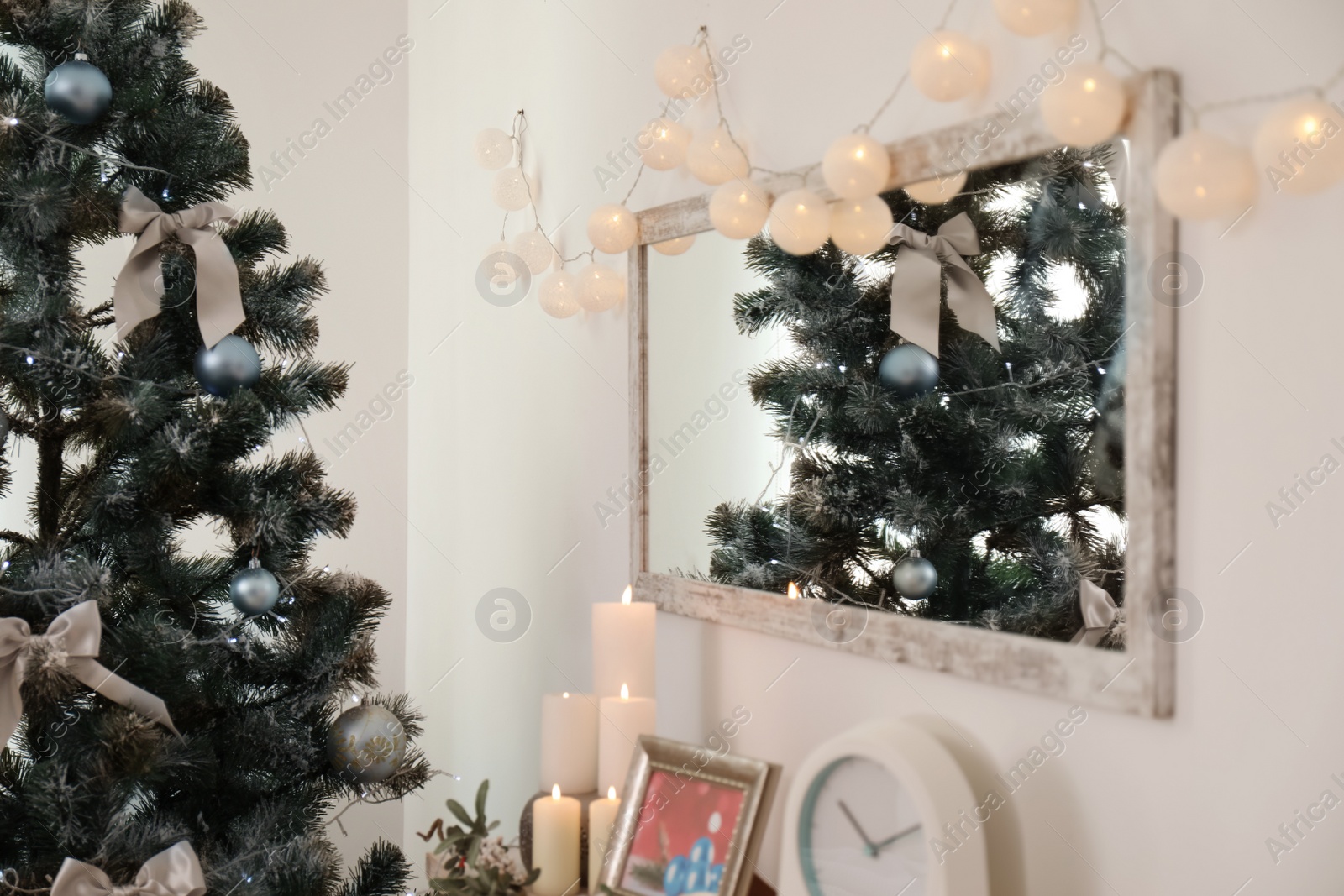 Photo of Mirror with Christmas lights on wall and decorated fir tree in stylish living room interior