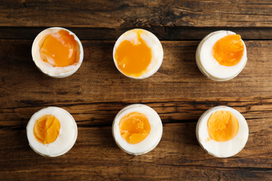 Photo of Different readiness stages of boiled chicken eggs on wooden table, flat lay