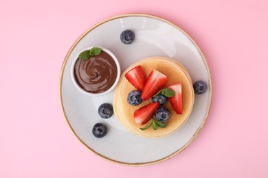 Photo of Delicious pancakes with strawberries, blueberries, mint and chocolate sauce on pink background, top view