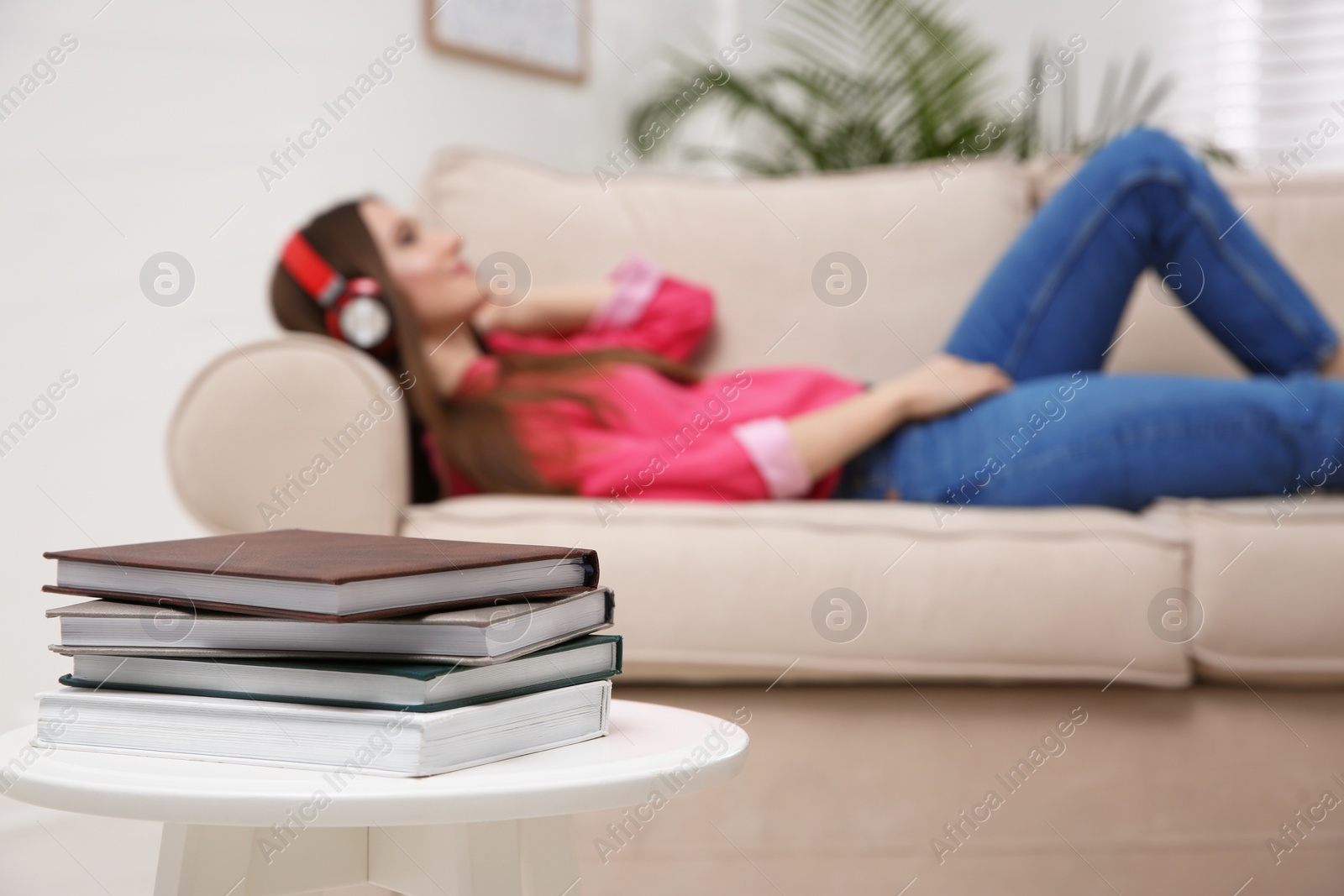 Photo of Stack of books on table at home and woman with headphones on background. Audiobook concept