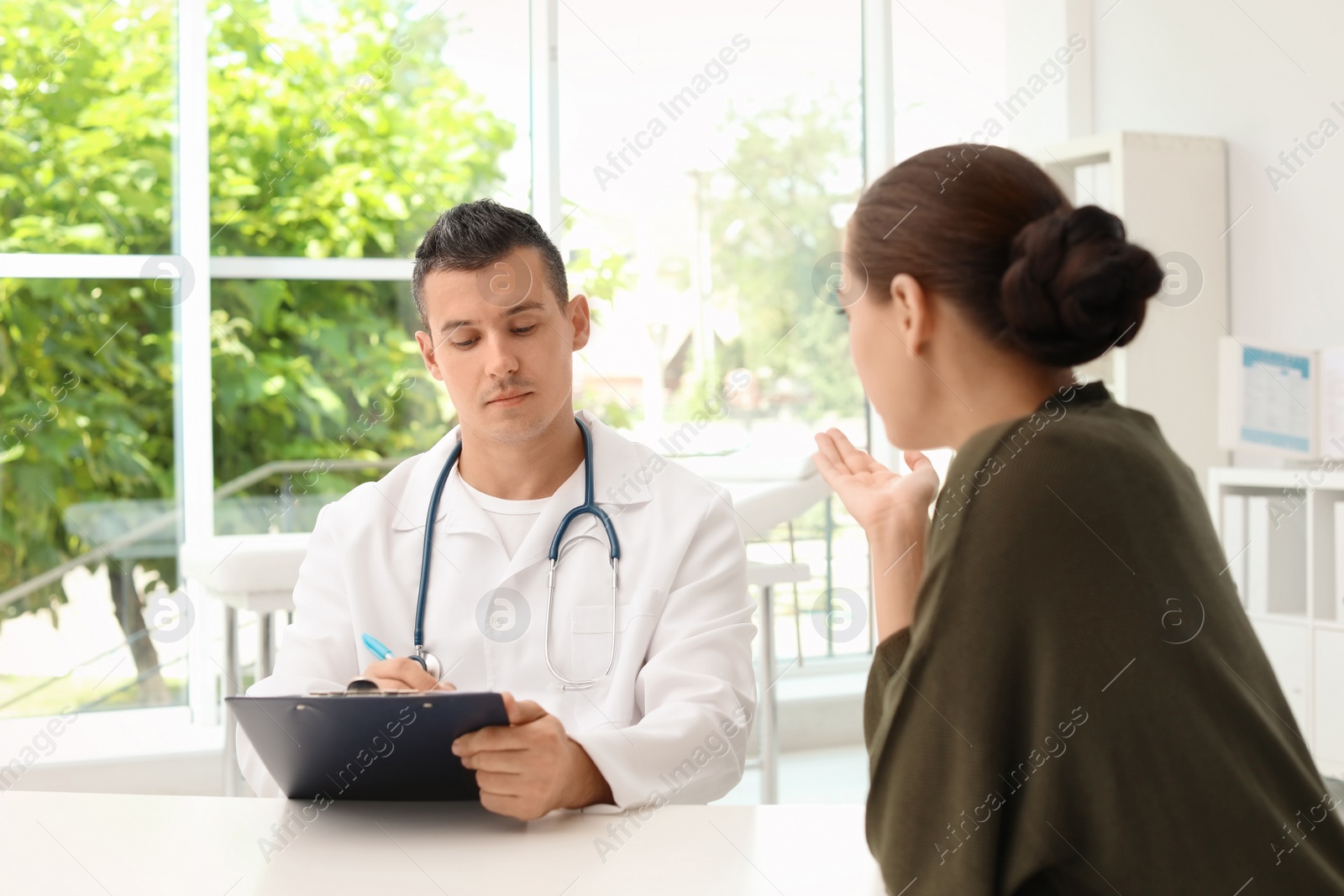 Photo of Young doctor listening to patient's complaints in hospital