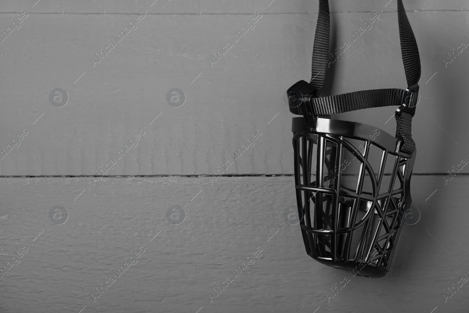 Photo of Black plastic dog muzzle on gray wooden table, top view, Space for text