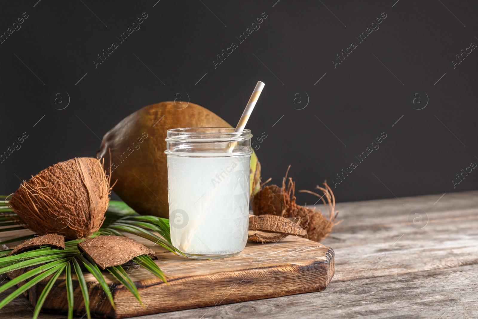 Photo of Beautiful composition with glass jar of coconut water on table against dark background