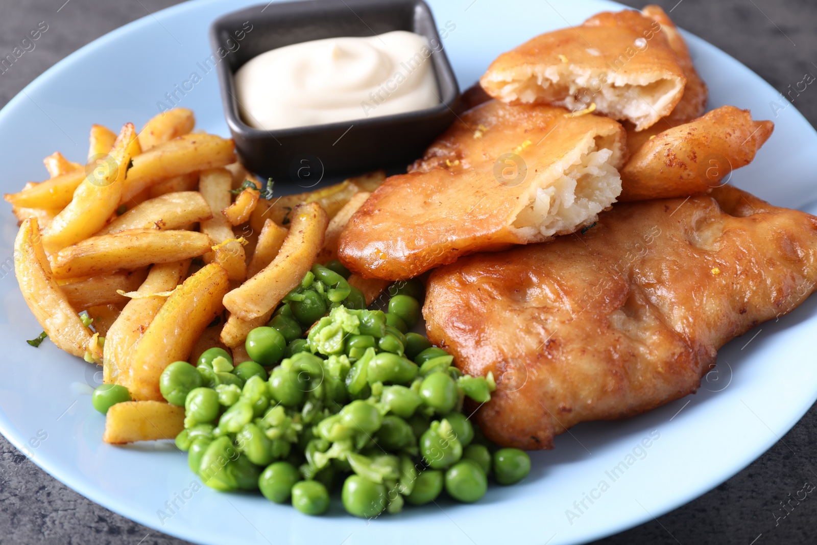 Photo of Tasty fish, chips, sauce and peas on grey table, closeup