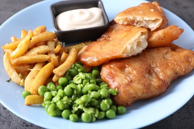 Photo of Tasty fish, chips, sauce and peas on grey table, closeup