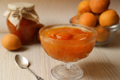 Photo of Dessert bowl with delicious apricot jam and spoon on white wooden table