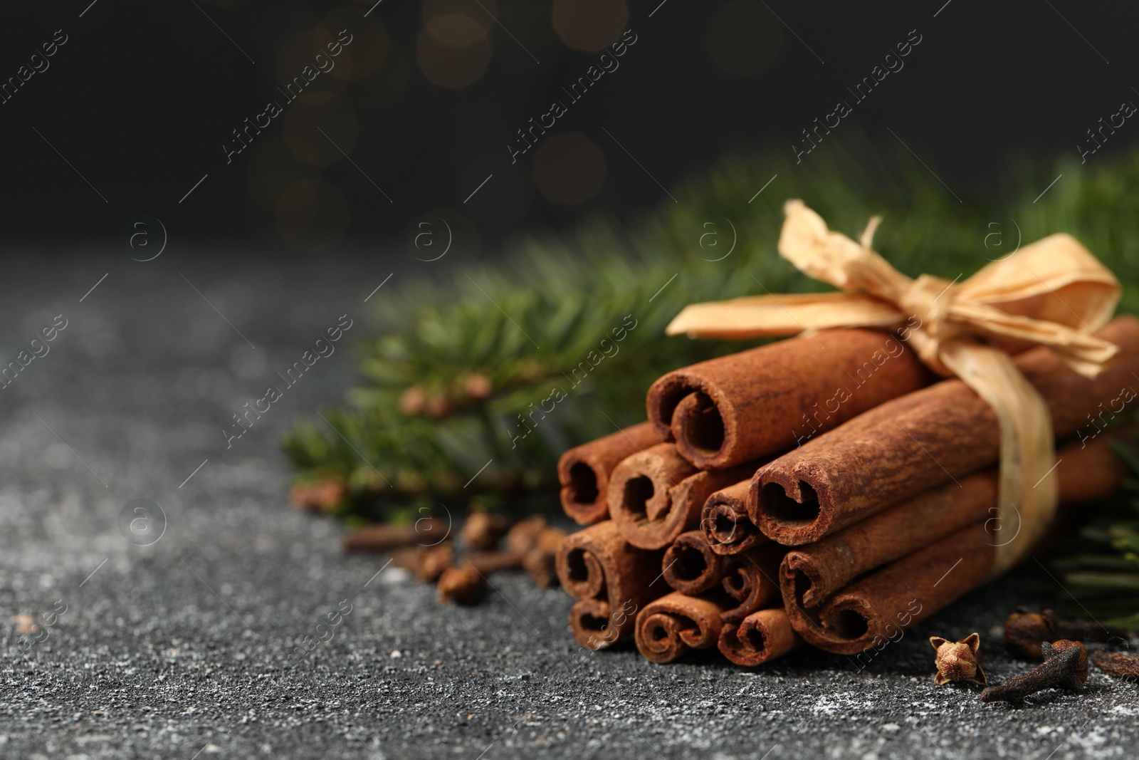 Photo of Different spices. Aromatic cinnamon sticks and clove seeds on dark gray textured table, closeup. Space for text