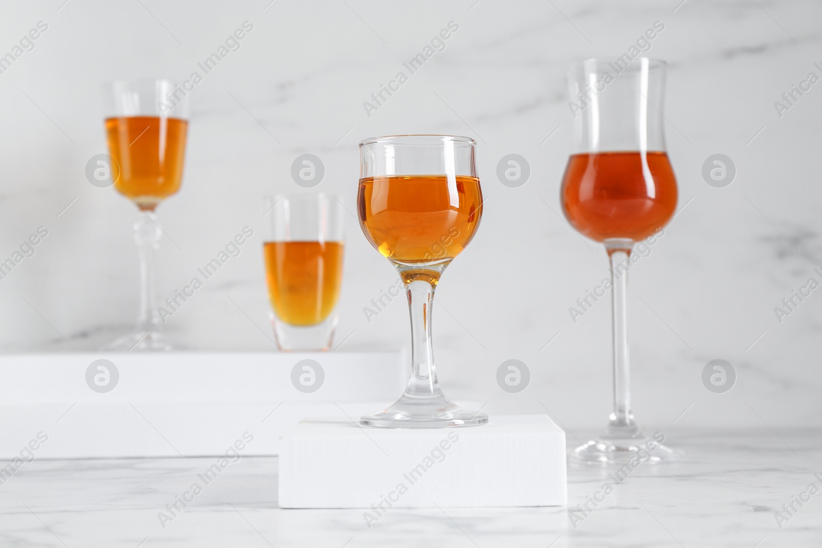 Photo of Different delicious liqueurs in glasses on white marble table