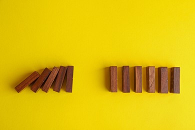 Photo of Falling and standing wooden domino tiles on yellow background, flat lay. Space for text