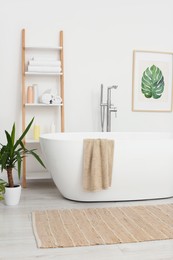 Photo of Stylish white tub and houseplant in bathroom. Interior design