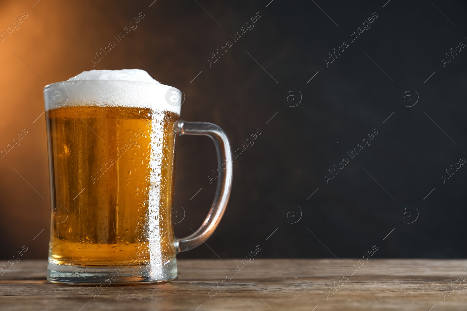 Photo of Cold tasty beer on wooden table against dark background. Space for text