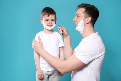 Photo of Dad pretending to shave his little son on color background