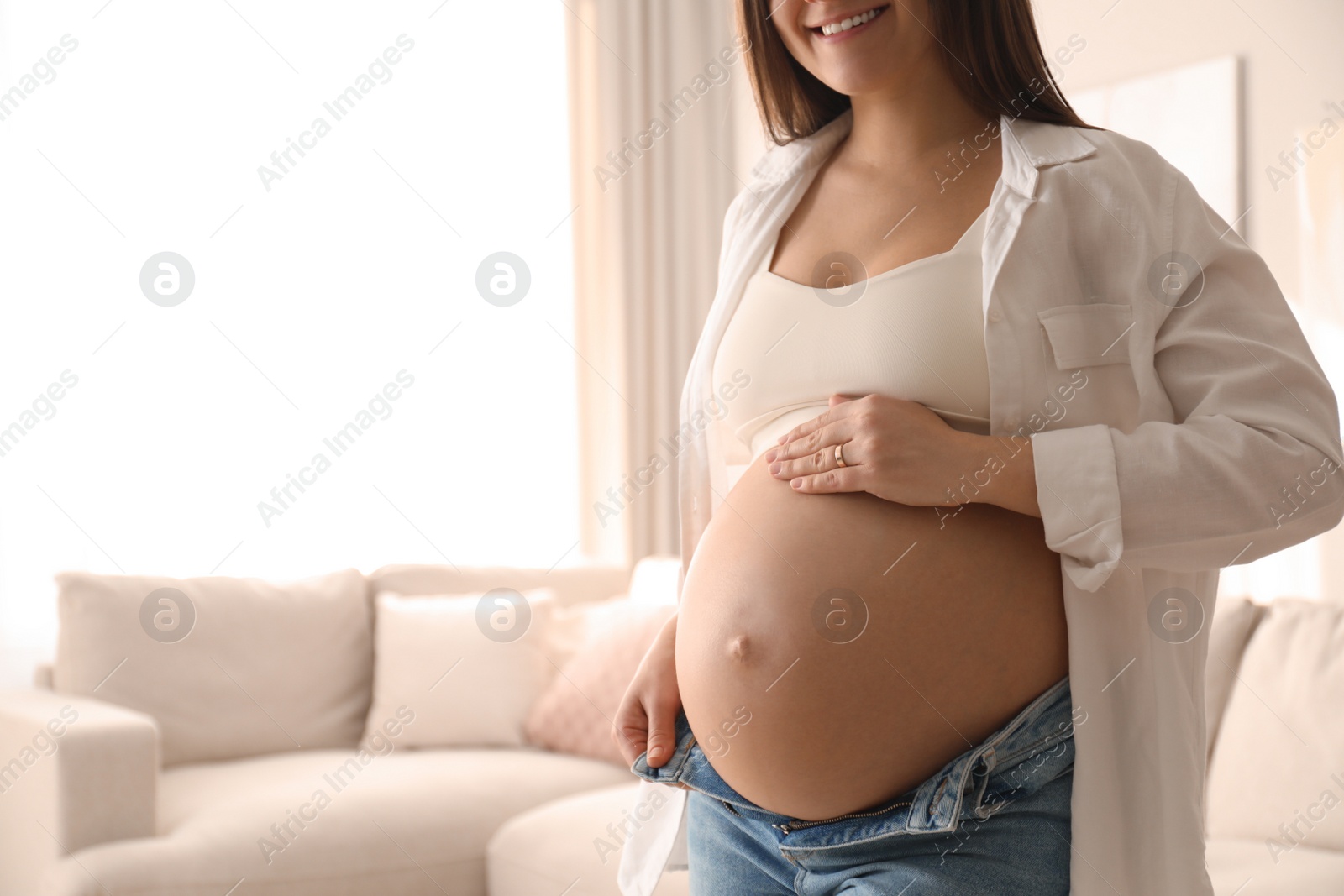 Photo of Pregnant young woman touching belly at home, closeup. Space for text