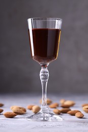 Liqueur glass with tasty amaretto and almonds on light grey table, closeup