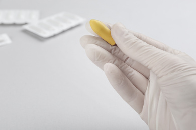 Photo of Woman holding suppository on light background, closeup. Hemorrhoid treatment