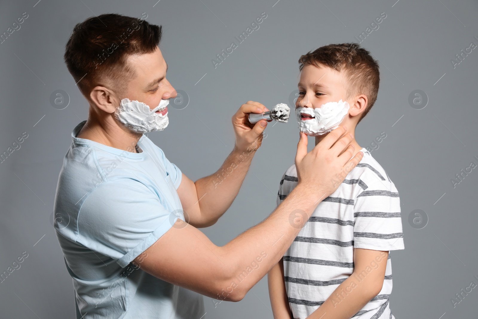 Photo of Dad applying shaving foam on son's face, grey background