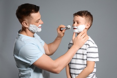 Dad applying shaving foam on son's face, grey background