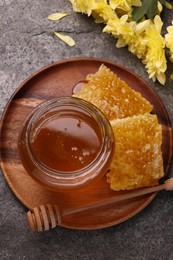 Photo of Sweet golden honey in jar, dipper, pieces of honeycomb and chrysanthemum flowers on grey textured table, flat lay