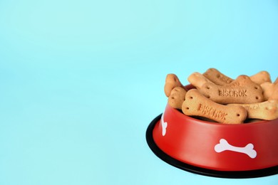 Bone shaped dog cookies in feeding bowl on light blue background, space for text