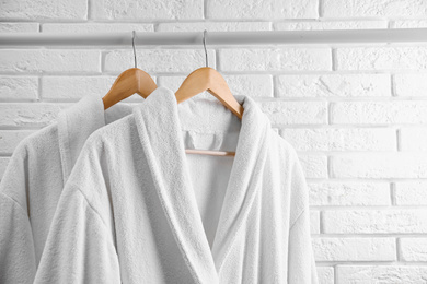Photo of Fresh bathrobes hanging on rack near white brick wall