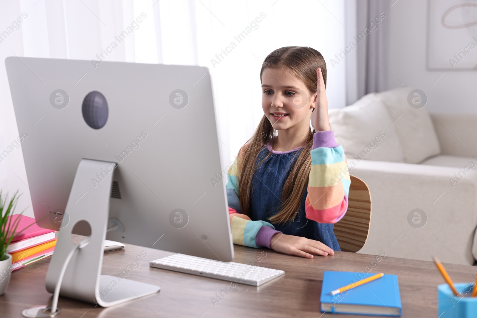 Photo of E-learning. Cute girl raising her hand to answer during online lesson at table indoors