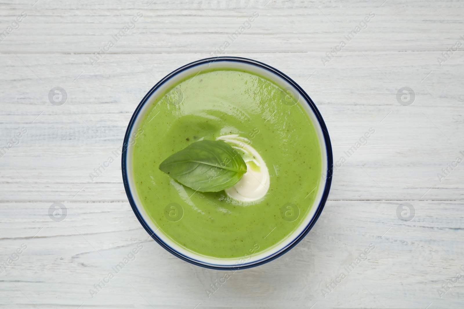 Photo of Tasty homemade zucchini cream soup on white wooden table, top view