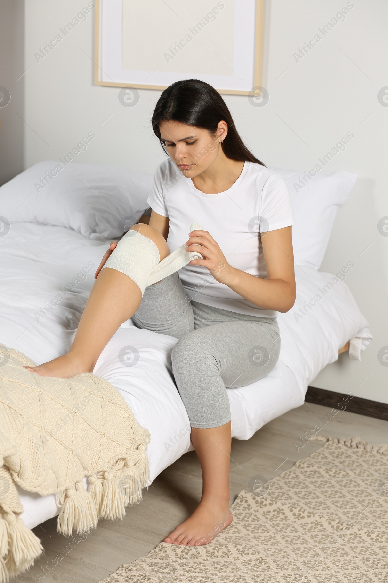 Photo of Young woman applying medical bandage onto knee in bedroom