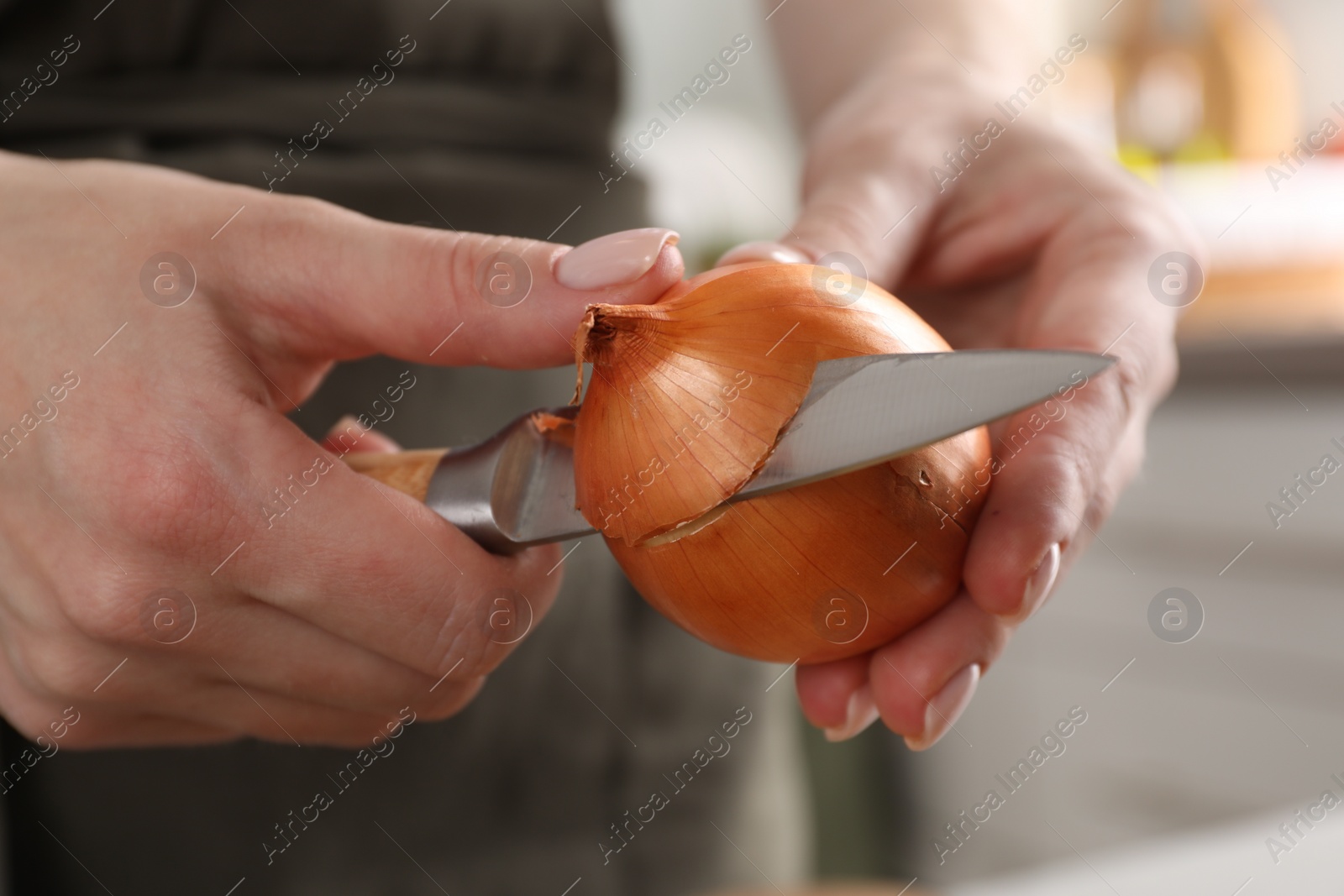 Photo of Woman peeling fresh onion with knife indoors, closeup