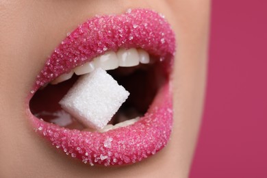 Closeup view of young with beautiful lips eating sugar cube on pink background