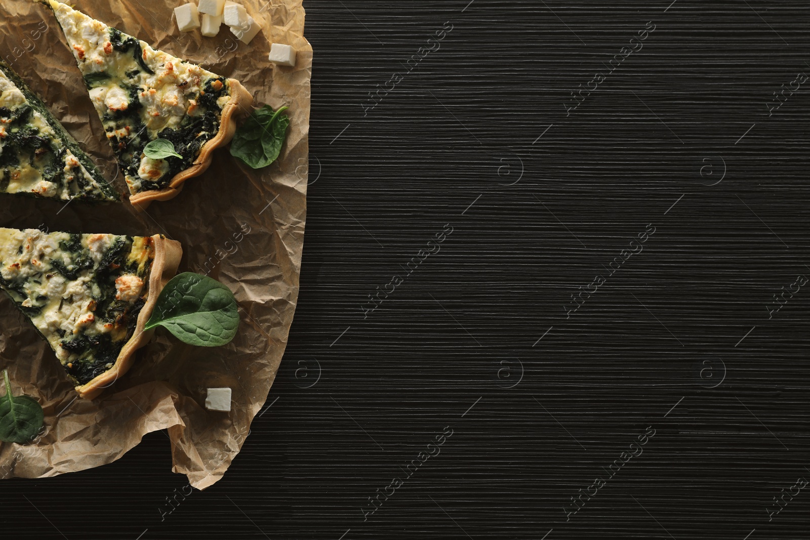 Photo of Delicious homemade spinach quiche on black wooden table, top view. Space for text