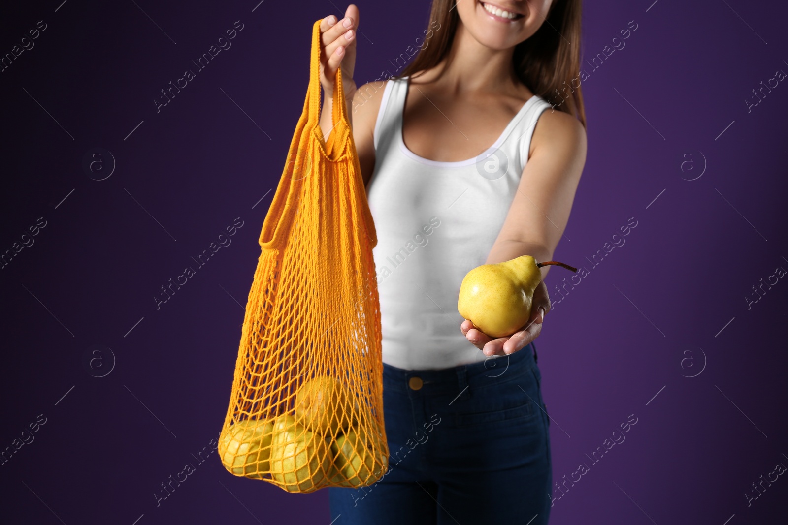 Photo of Woman holding net bag with fresh ripe pears on purple background, closeup