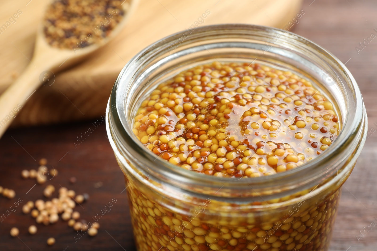 Photo of Whole grain mustard in jar on wooden table, closeup